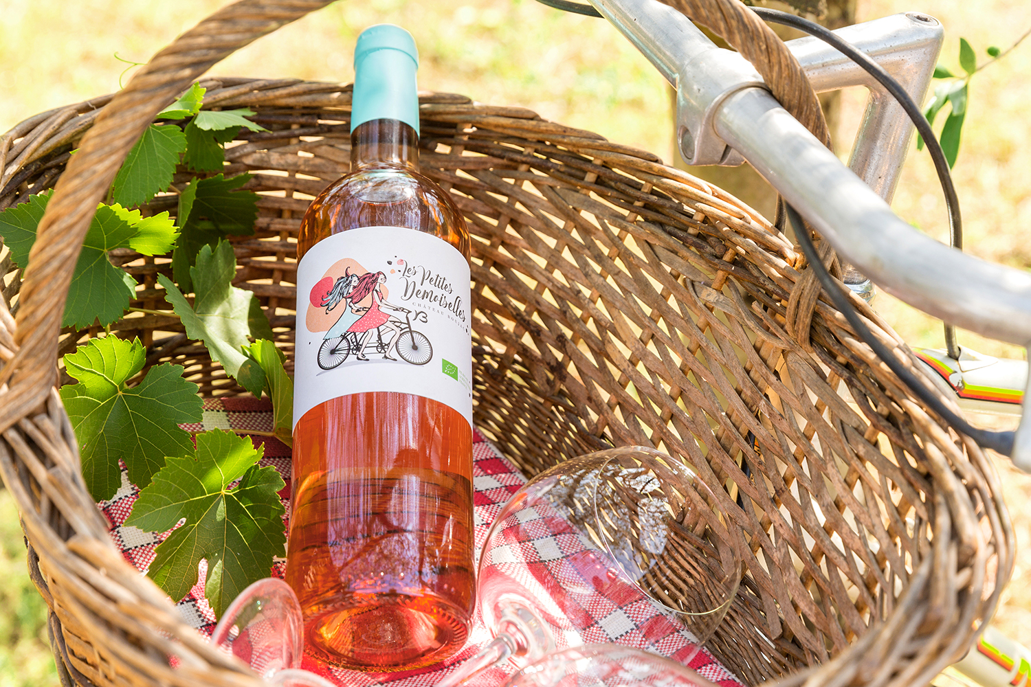 Photographie en situation pour un vignoble d'une bouteille de vin rosé dans un panier sur un vélo